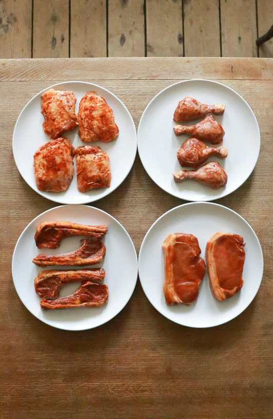 Plates of various fresh raw meat cuts with spices ready for a braai